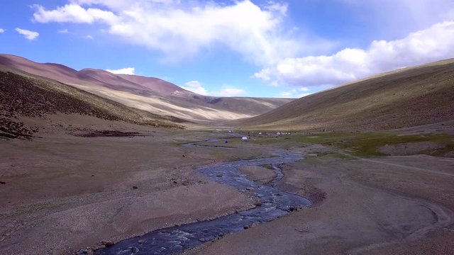 Aerial shot of a camp in the Himalayas, colorful tents, yacks, horses grazing at the Markha River