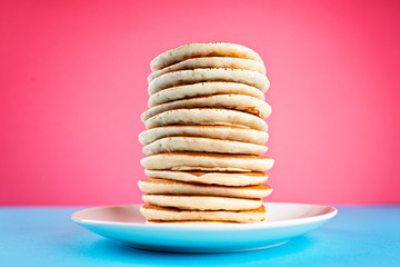 High stack of pancakes on pink and blue background