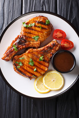 Barbecue pork chop in a tamarind sauce, with lemon and tomatoes close-up on a plate. Vertical top view