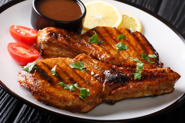 Grilled pork steak with bone in tamarind sauce, with lemon and tomatoes close-up on a plate. horizontal