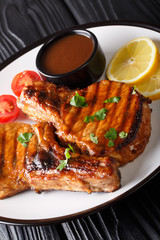 Grilled chop pork with tamarind sauce, served with lemon and tomatoes close-up on a plate. vertical