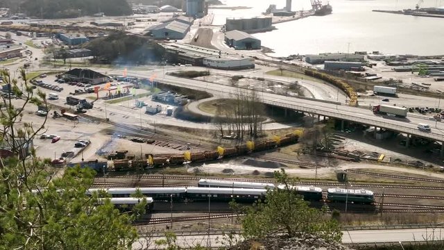 Aerial clip of Freight train slowly moving along tracks amidst a busy highway in Uddevalla Sweden