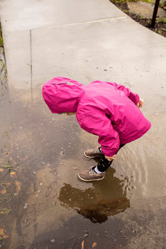 A preschool aged girl playing outdoors on a rainy day with a colorful rain jacket on.