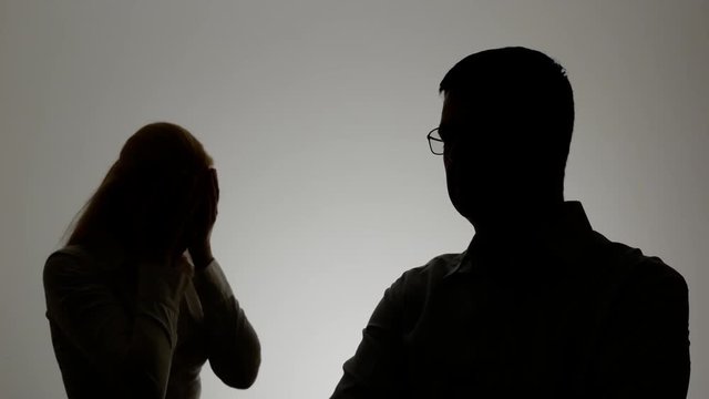 Silhouette of a man and a woman. Family quarrel, the woman shouts at the man and emotionally gesticulating hands,