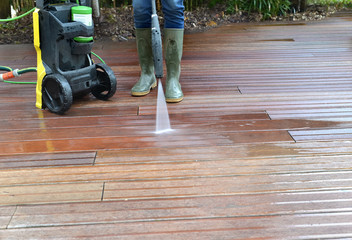 woman washing wooden terrace with high pressure water
