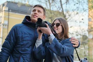 Young happy couple walking through the streets spring city, attractive male and female tourists taking pictures with photo camera