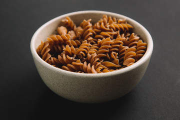 Whole grain fusilli on dark background, close up