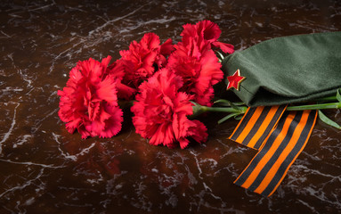 on the background of the monument, a bouquet of red carnations, military cap and St. George ribbon, close-up
