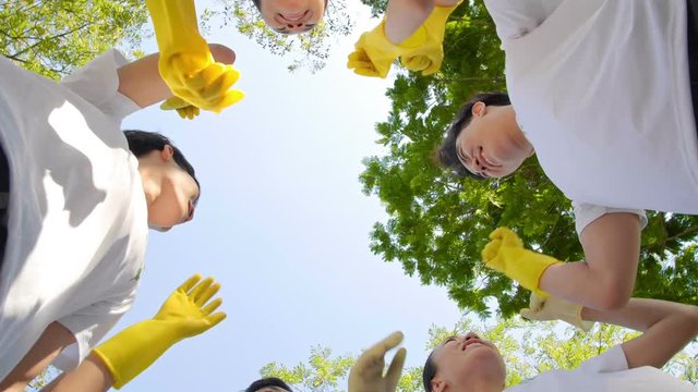 Directly below view of volunteer team standing outdoors, stacking hands in rub gloves together, then hugging altogether