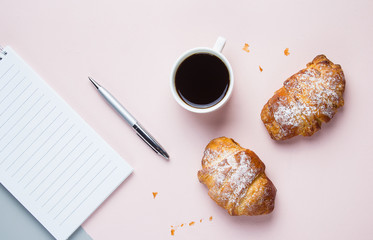 Coffee mug with croissants and empty notebook and pen for business plan and design ideas on pink background from above. Morning plan. Flat lay concept