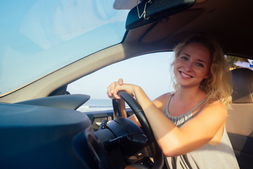 Young woman sitting in car and talking on the phone sunset on the waterfront.