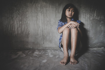 Sad little girl sitting against the wall in despair.