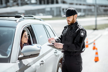 Policeman checking documents of a young female driver standing near the car on the roadside in the...