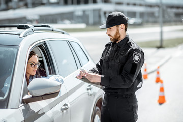 Policeman checking documents of a young female driver standing near the car on the roadside in the city