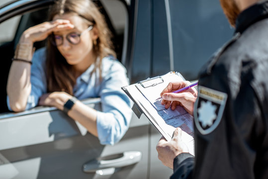 Policeman Issuing A Fine For Violating The Traffic Rules To A Young Woman Driver