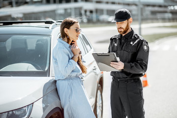 Policeman standing with female driver while issuing a fine for violating the traffic rules on the roadside near the car