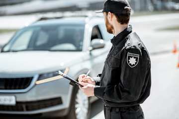 Obraz premium Policeman issuing a fine for violating the traffic rules standing in front of the car on the roadside
