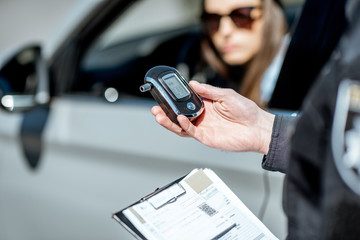 Policeman holding device for checking alcohol intoxication while standing near the stopped car with...