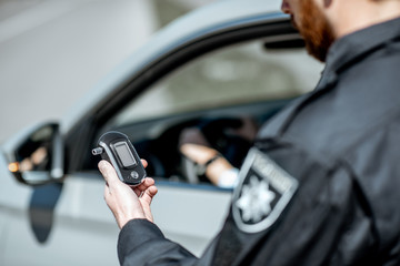 Policeman holding device for checking alcohol intoxication while standing near the stopped car with...
