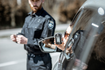 Policeman checking woman driver for alcohol intoxication with special device while stopped for...