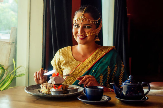 Portrait Of A Indian Woman In Green Sari And Gold Jeweler Looking At Pancakes With Whipped Cream And Strawberries Dessert, Eager To Eat.