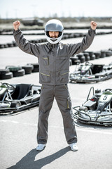 Full body portrait of a happy racer in protective sportswear standing as a winner of a go-kart race outdoors