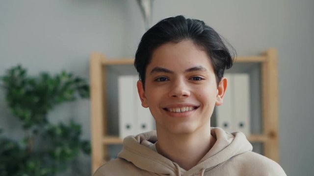 Close-up slow motion portrait of good-looking teenager with thendy hairstyle looking at camera and smiling. Happy childhood, cheerful people and house concept.