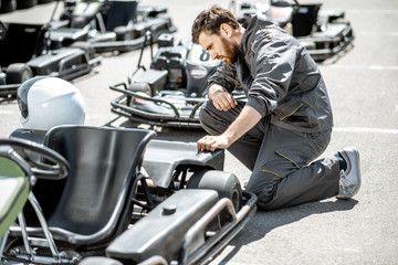 Fototapeta na wymiar Racer or repairman in uniform serving go-kart machine before racing on the track