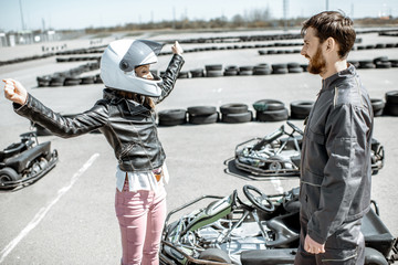 Happy female driver with instructor on the go-kart track outdoors - obrazy, fototapety, plakaty