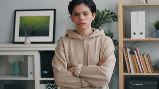 Portrait of serious teenager in trendy hoodie looking at camera with straight face standing alone at home. Young people, interior and modern lifestyle concept.