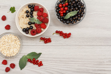 Oatmeal porridge in porcelain bowl with currant berries and raspberries, decorated with mint leaves.