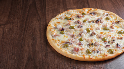 Pizza with seafood and olives on a wooden table next to the copy space.