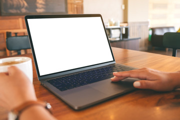 Mockup image of a woman using and touching on laptop touchpad with blank white desktop screen on wooden table while drinking coffee