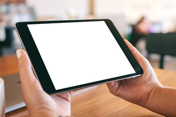 Mockup image of hands holding black tablet pc with blank white screen with laptop and coffee cup on wooden table