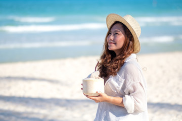 Portrait image of a beautiful asian woman holding and drinking coconut juice on the beach