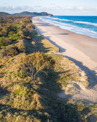 Aerial shot at sunrise over the ocean, sand beach with swimmers and surfers enjoying summer. Byron...