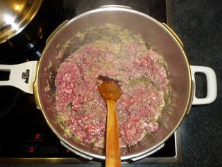Close up top down view cooking frizzle homemade fresh minced meat at a large aluminum pot in an oven with wooden spatula