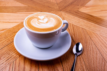 White coffee cup with heart shape latte art foam on wood table.