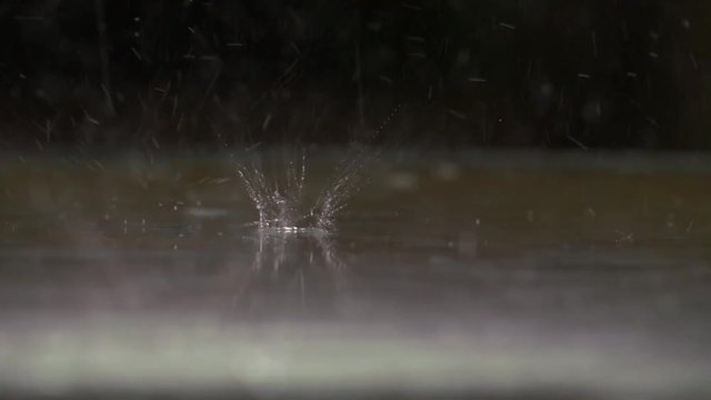 Heavy rain patters in slow motion on a glass roof, which is illuminated from below taken with 180p.