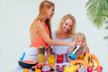 mother and daughter drinking smoothies together at summer tropical vacation.three female making drinking fresh juice in glass smoothies blender papaya, pineapple, watermelon, dragonfruit ingredient