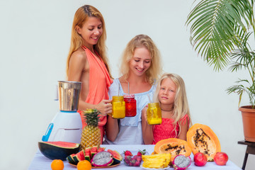 mother and daughter drinking smoothies together at summer tropical vacation.three female making drinking fresh juice in glass smoothies blender papaya, pineapple, watermelon, dragonfruit ingredient