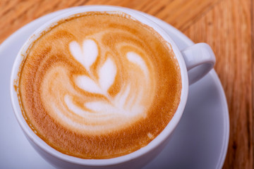 Latte hot coffee or cappuccino in a white cup with latte art on wooden table background.