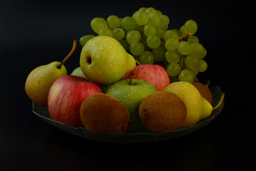 Fototapeta na wymiar Still life on a black background.Fruit on black background.Apples pears kiwi grapes lemon.Healthy and healthy food. Bright fruit.Healthy diet. Natural food.