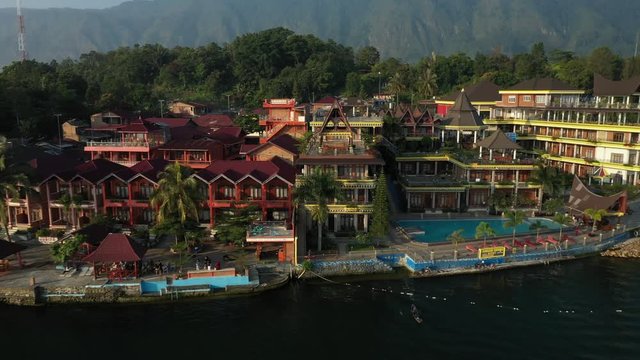 Pullback drone footage of a traditional Batak roof structure on a lakeside resort on Lake Toba in North Sumatra, Indonesia.