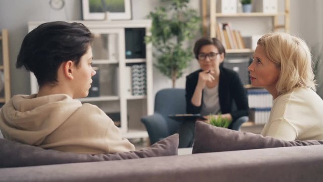 Mature lady discussing relationship with teenage son while psychologist is giving advice during session in office. Family, unhappiness and psychology concept.