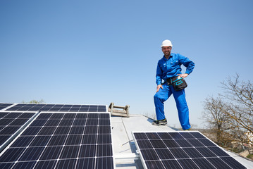 Man engineer in blue suit and protective helmet installing solar photovoltaic panel system. Smiling...