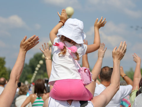 A Little Girl Sits On The Neck Of A Man Raising His Hands Up