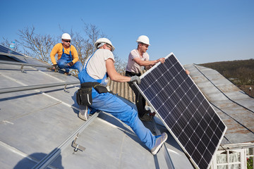 Male workers installing solar photovoltaic panel system. Electricians lifting blue solar module on...