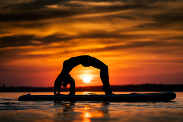 Young woman exercising on paddle-board at sunset.