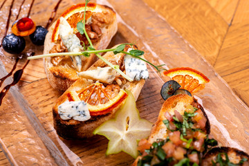 Appetizer bruschetta with cheese, honey, walnut and dry orange slices on wooden table. Close-up.